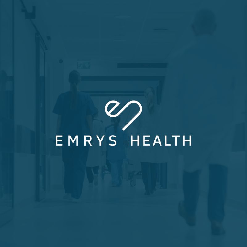 Emrys health dark blue image with white Emrys Health logo in the middle healthcare setting in the background.