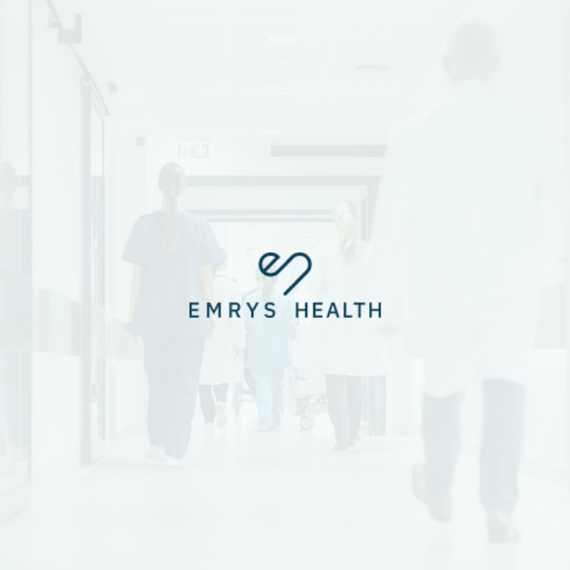 Emrys health white image with white Emrys Health logo in the middle healthcare setting in the background.